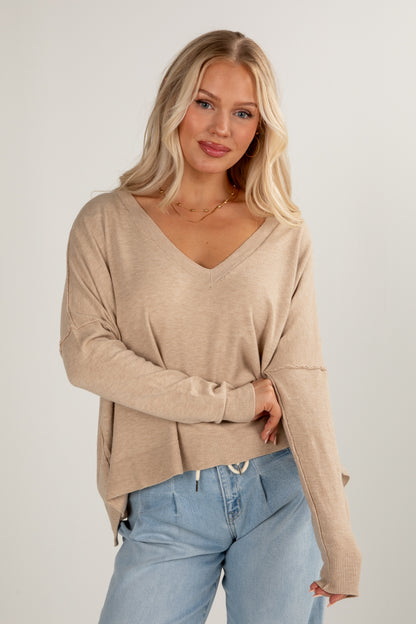 Woman wearing a beige sweater and light blue jeans against a plain background