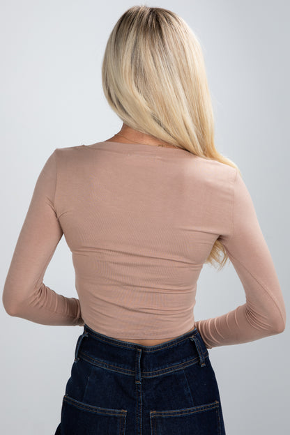 Person wearing a beige long-sleeve top and dark jeans on a plain background