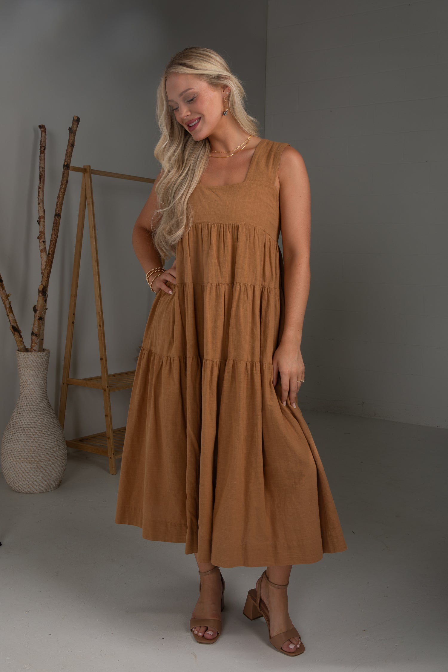 Woman wearing a brown dress standing in a studio setting with a neutral background