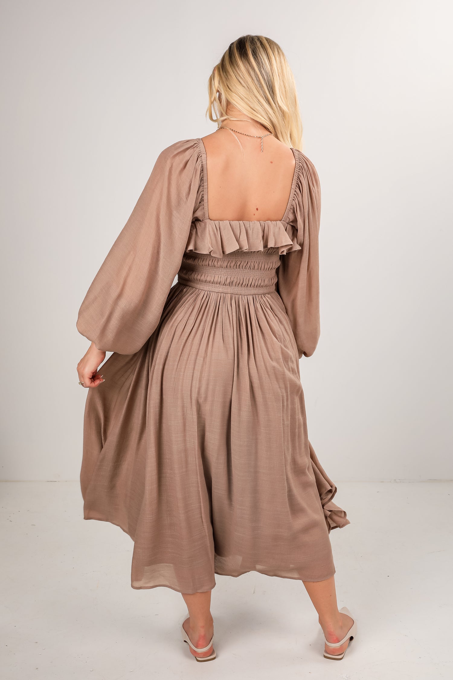 Woman wearing a beige dress with long sleeves on a white background