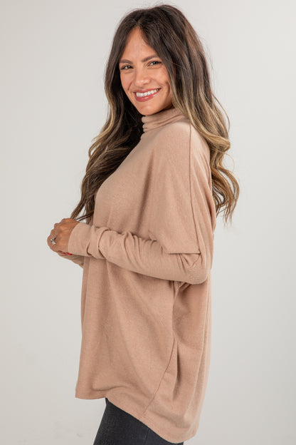 Woman wearing a beige long-sleeve top against a plain background