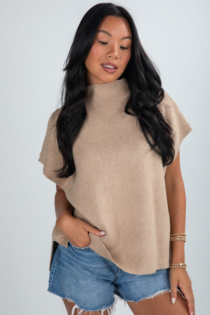 Woman wearing a beige sleeveless sweater and denim shorts on a white background