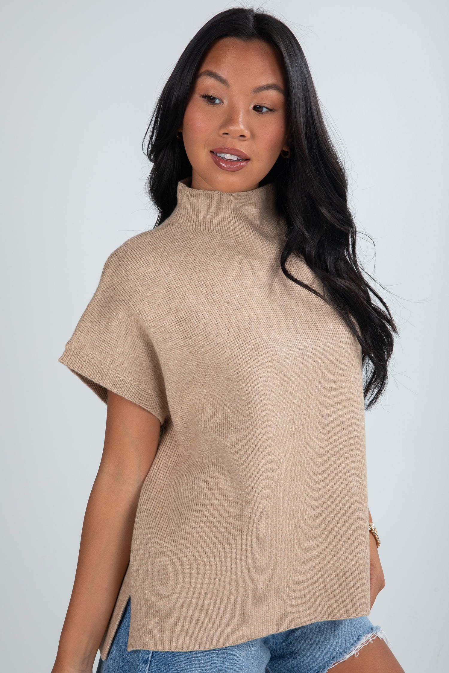 Woman wearing a beige turtleneck sweater over a blue top against a plain background