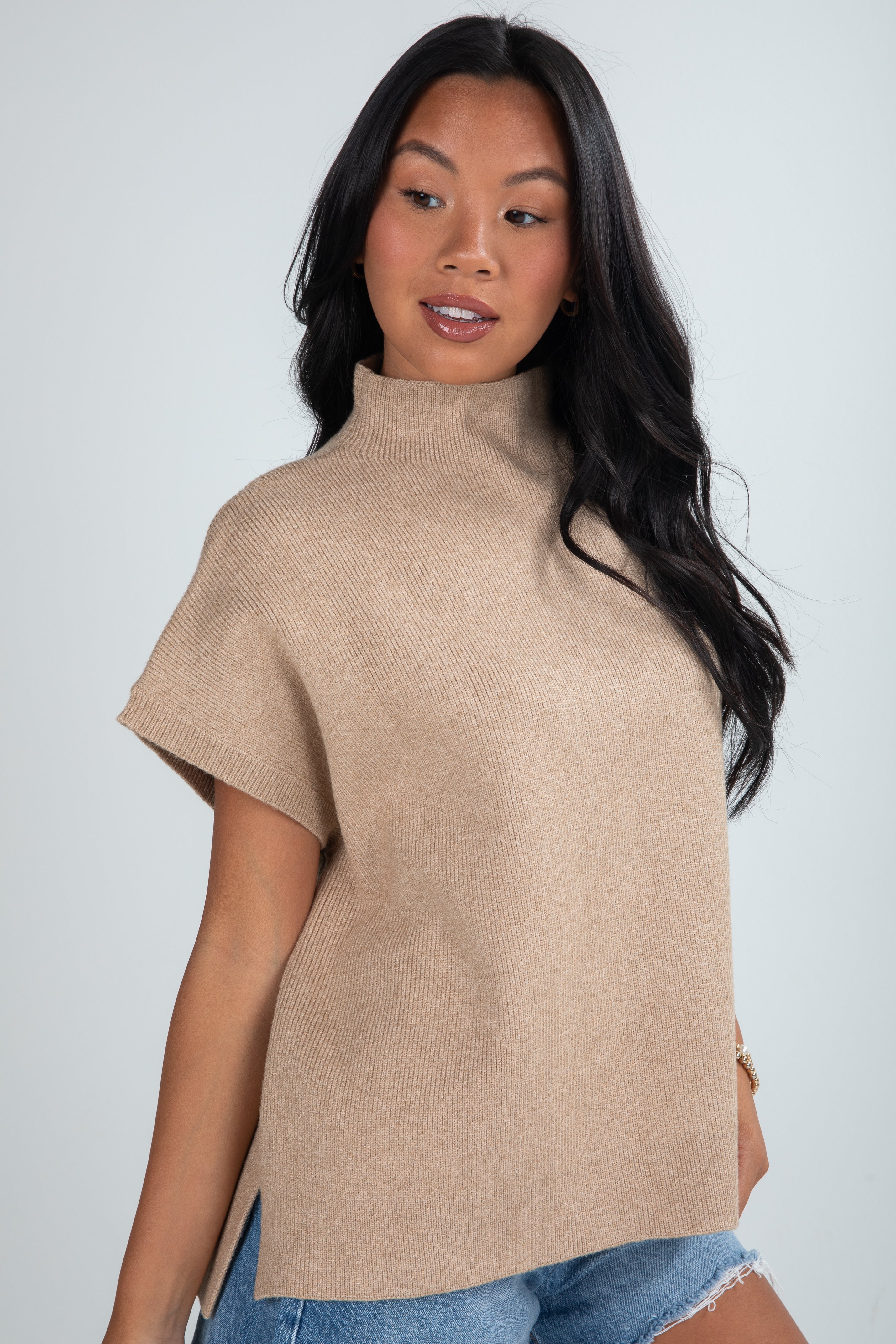 Woman wearing a beige turtleneck sweater over a blue top against a plain background