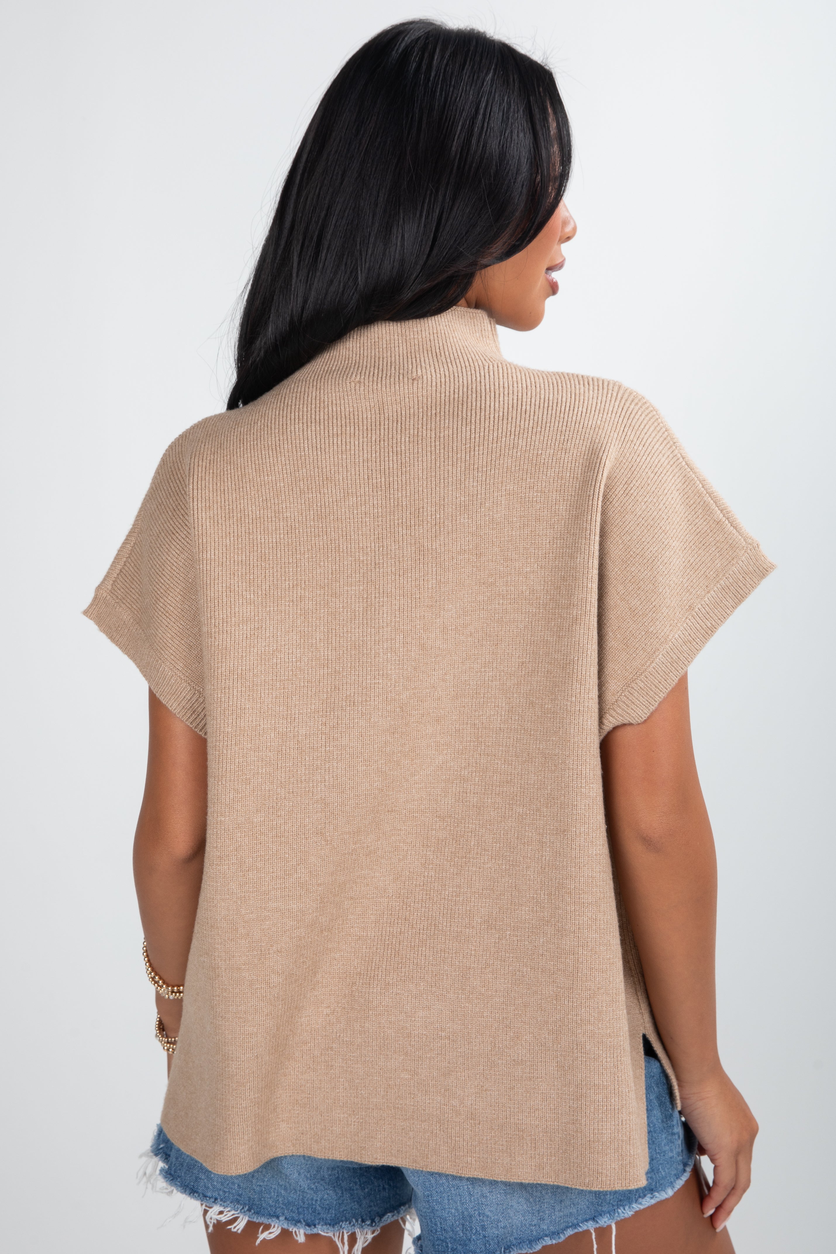 Woman wearing a beige cardigan over denim shorts on a white background