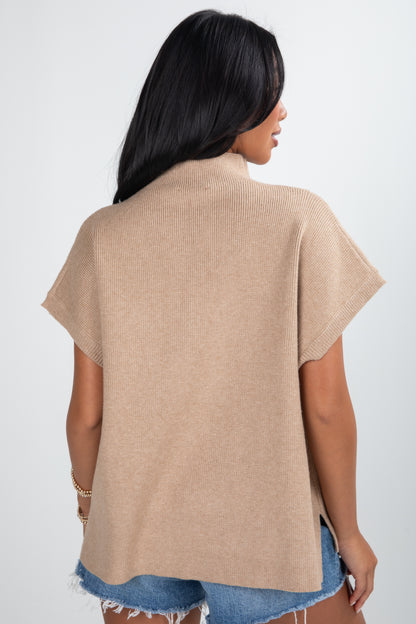 Woman wearing a beige cardigan over denim shorts on a white background