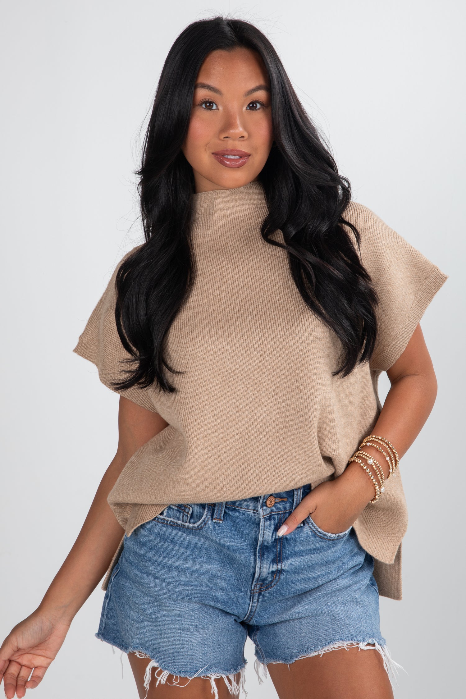 Woman wearing a beige sweater and denim shorts on a white background