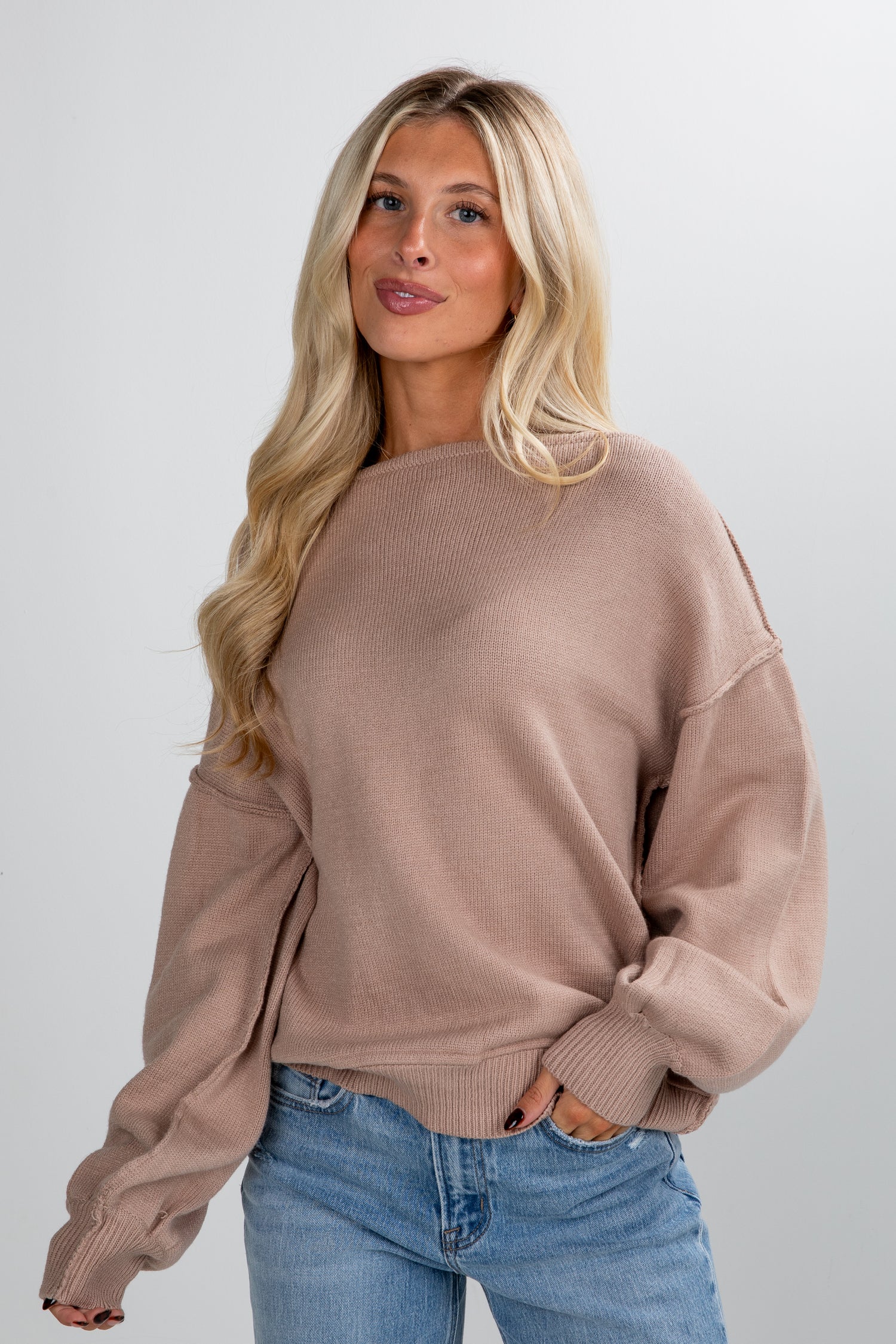 Woman wearing a beige sweater and blue jeans against a plain background
