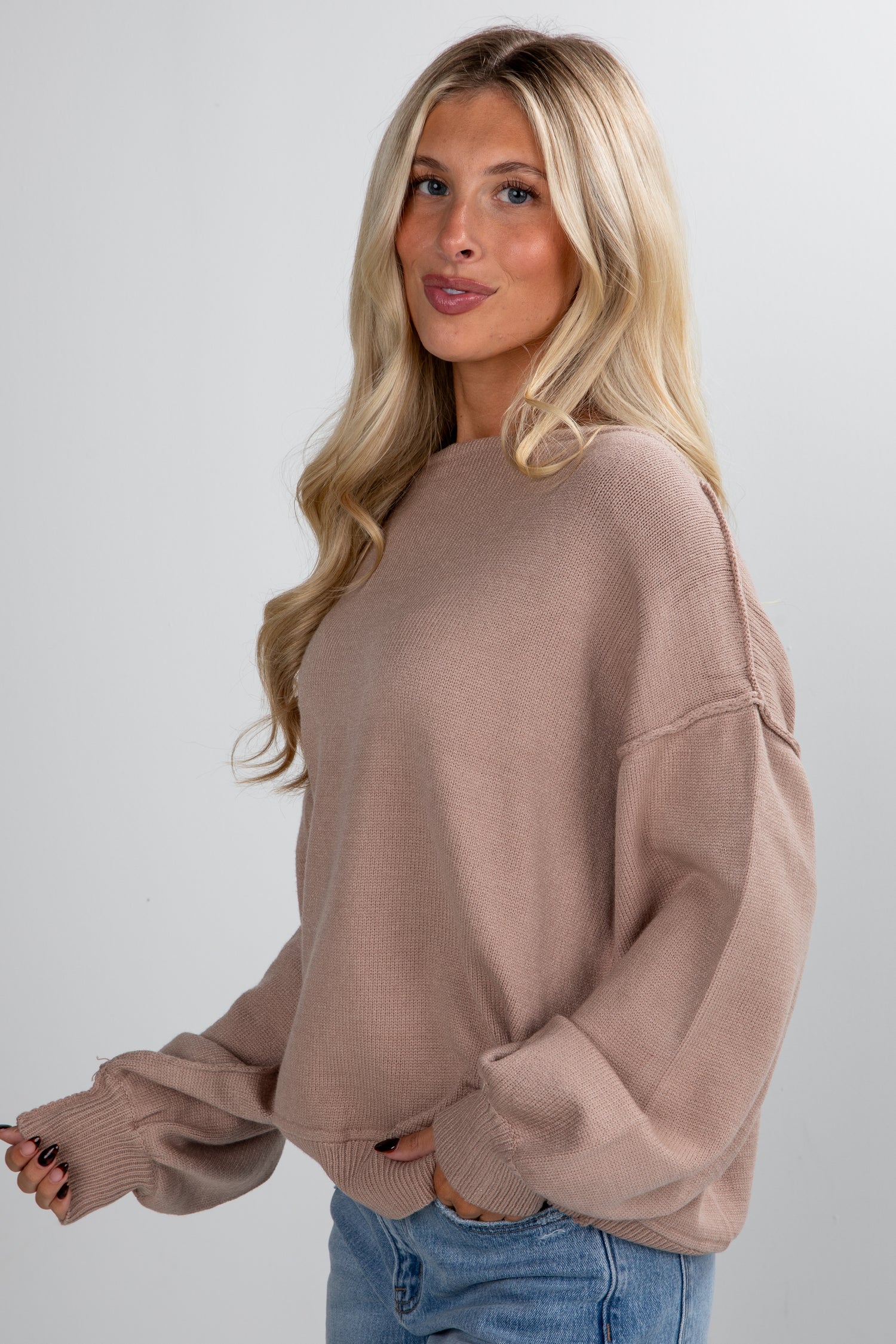 Woman wearing a brown sweater and blue jeans against a plain background