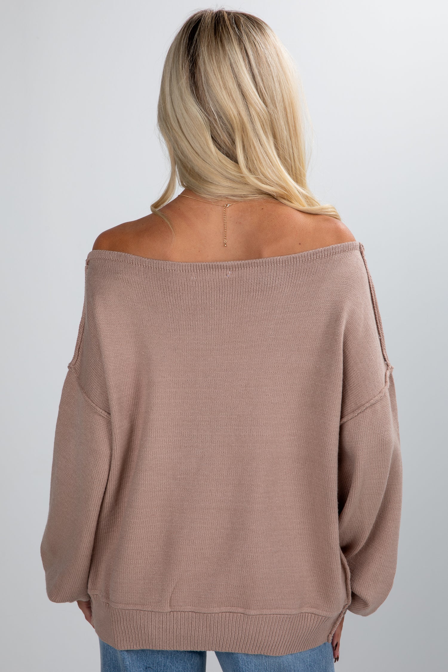 Person wearing a brown off-shoulder sweater on a plain background
