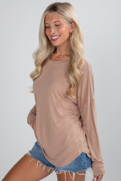 Woman wearing a beige long-sleeve top and denim shorts on a plain background