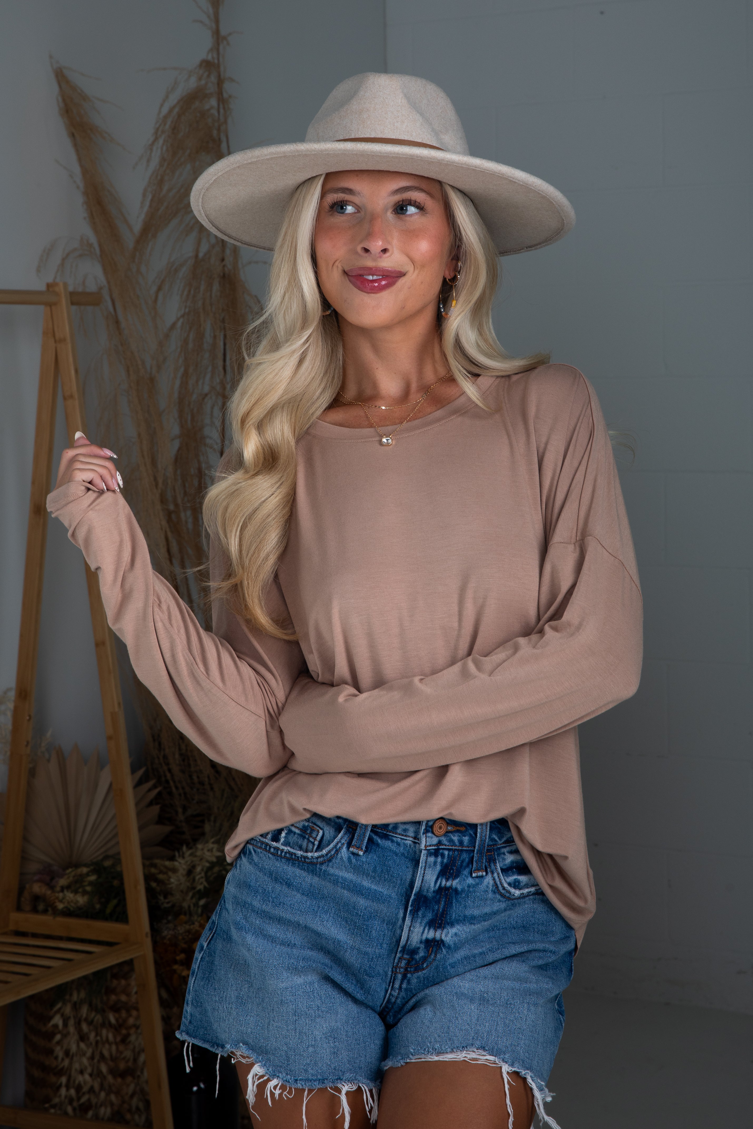 Woman wearing a beige hat, long-sleeve top, and denim shorts indoors.