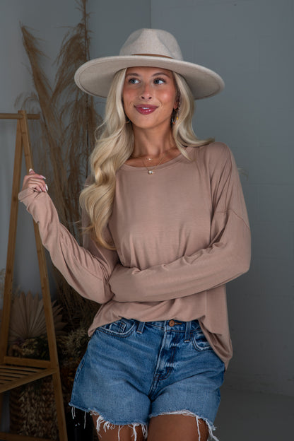 Woman wearing a beige hat, long-sleeve top, and denim shorts indoors.