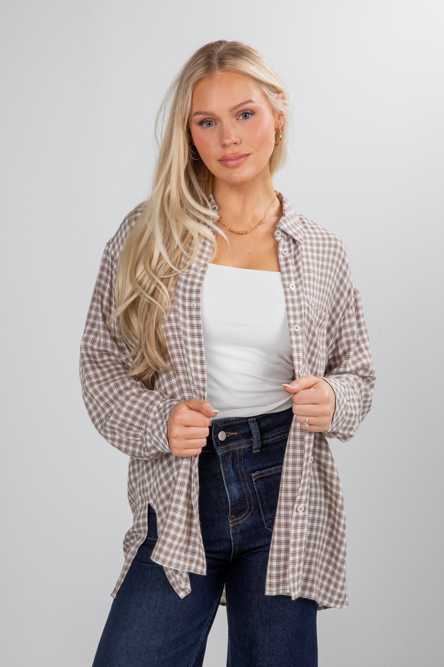 Woman wearing a plaid shirt over a white top and jeans on a plain background
