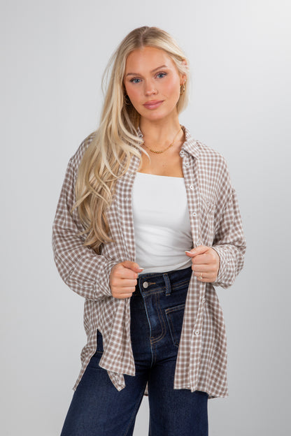Woman wearing a plaid shirt over a white top and jeans on a plain background