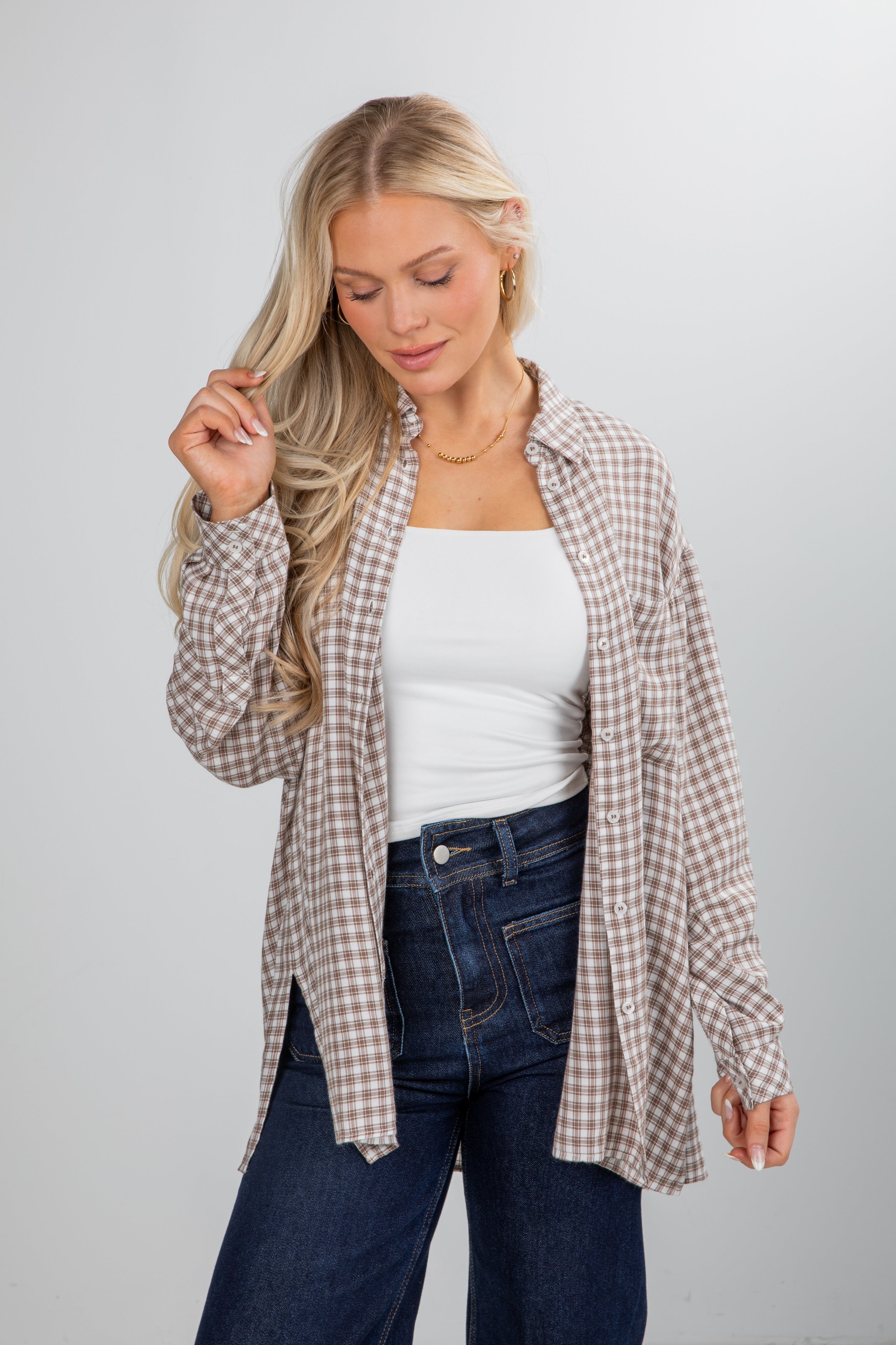 Woman wearing a plaid shirt over a white top and jeans on a gray background