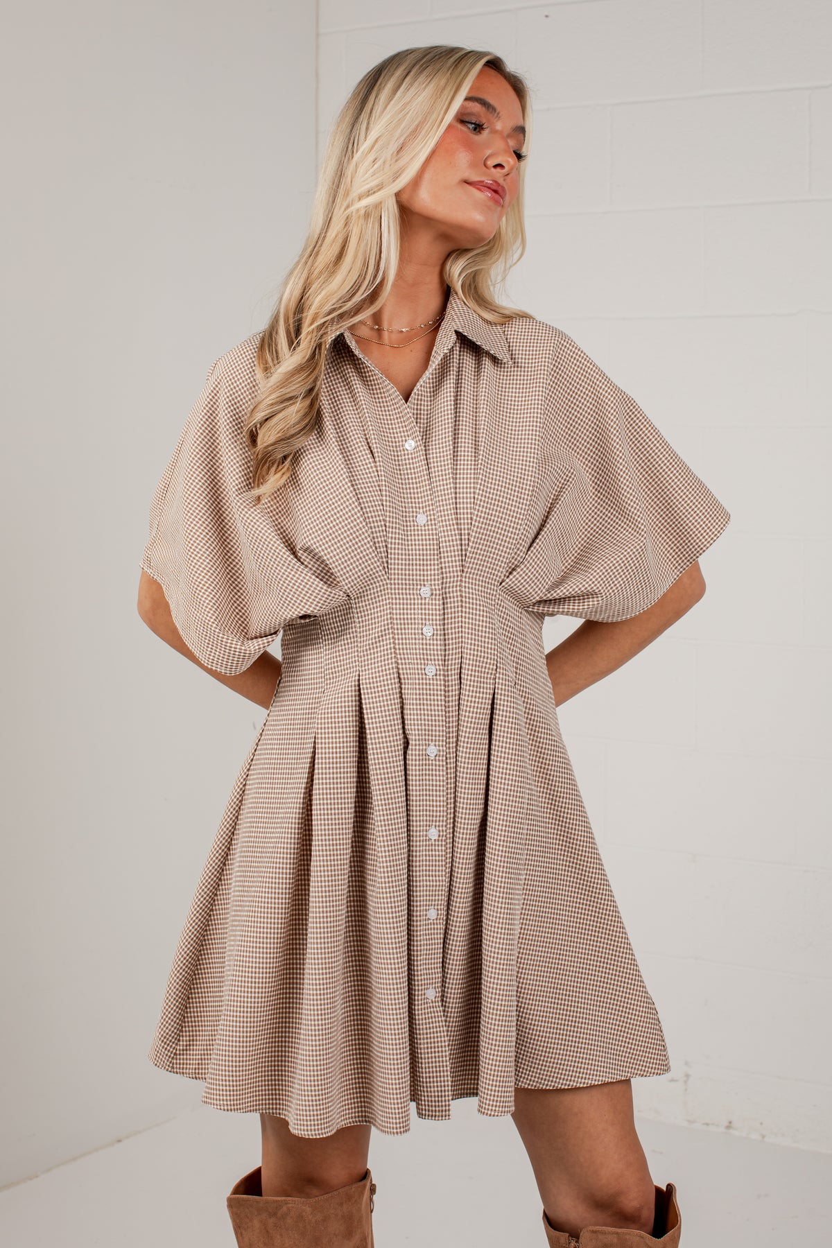 A woman modeling a beige and white striped short-sleeve button-up dress with a flared skirt, paired with brown boots, against a white studio background.