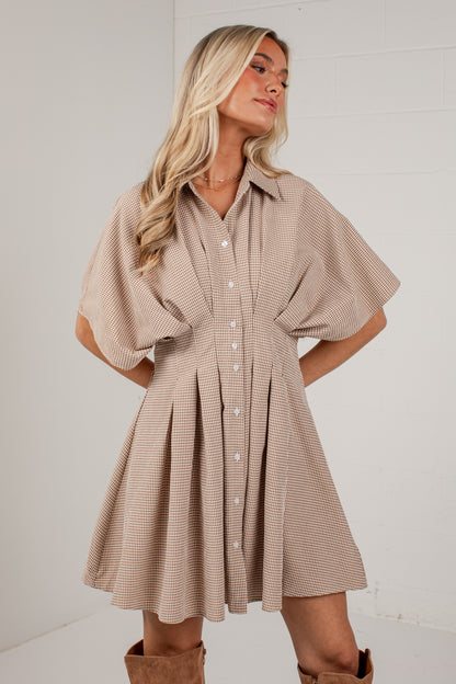 A woman modeling a beige and white striped short-sleeve button-up dress with a flared skirt, paired with brown boots, against a white studio background.