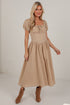 A woman modeling a beige midi dress with puff sleeves, a square neckline with gathered ruffles, and a flared skirt, paired with brown suede ankle boots against a white studio background.