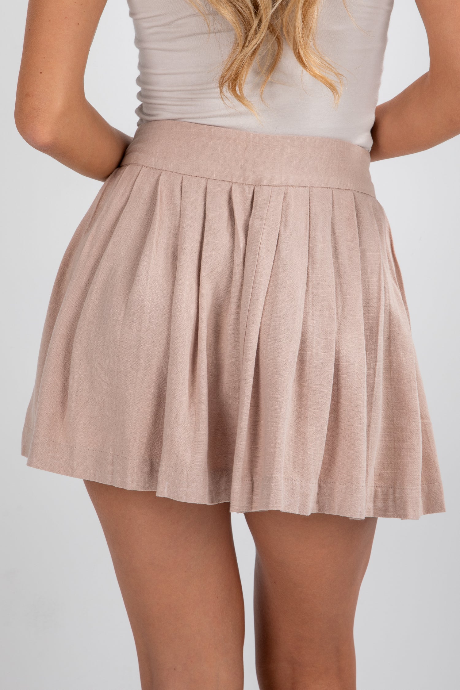 Beige pleated skirt worn by a person on a white background