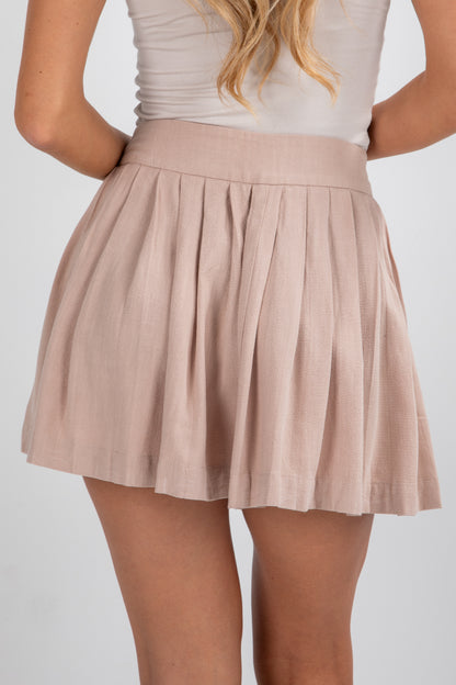 Beige pleated skirt worn by a person on a white background