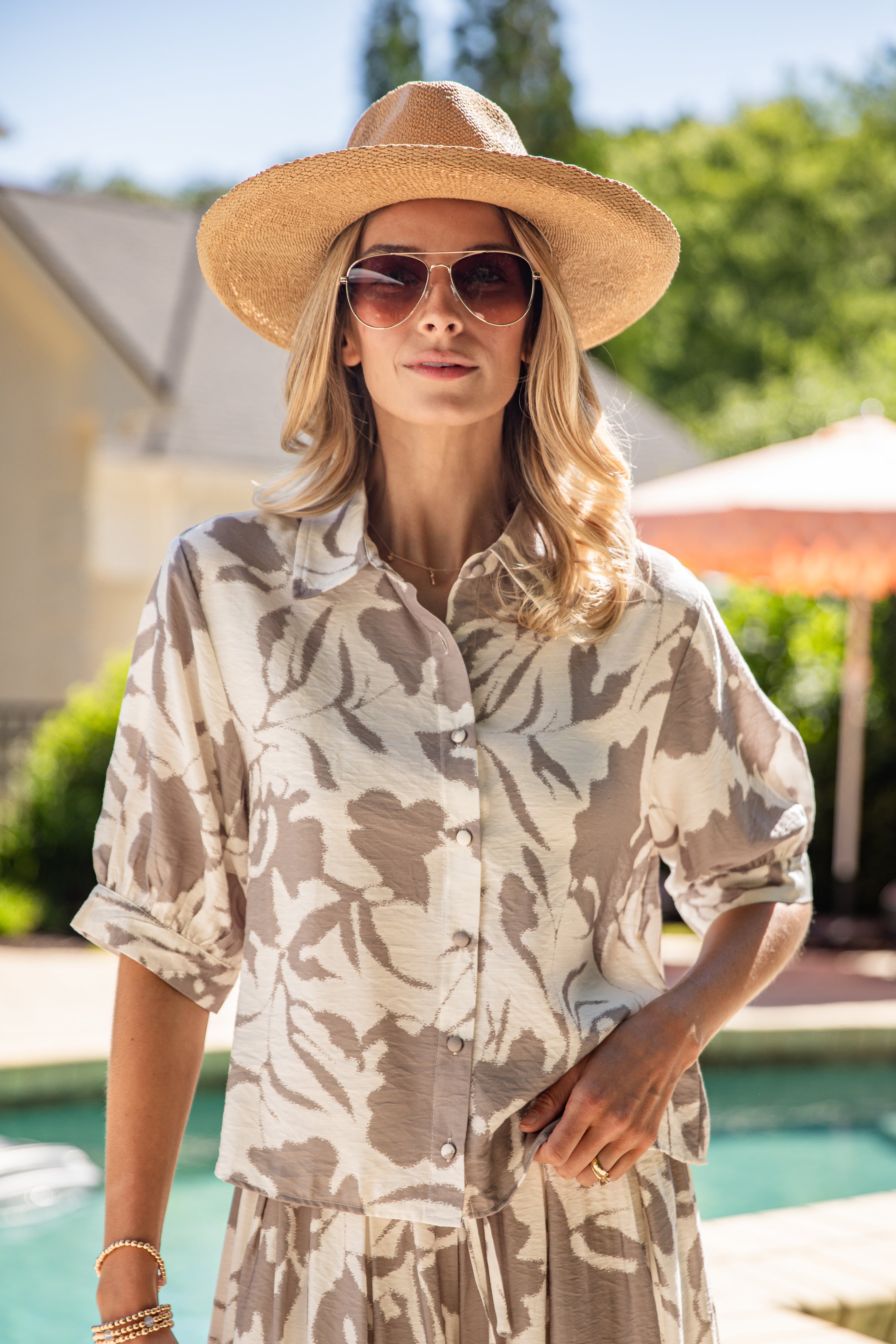 Woman wearing a patterned shirt and sun hat by a poolside
