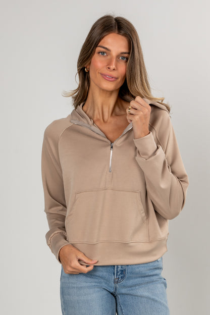 Woman wearing a beige pullover with a zipper on a plain background