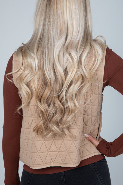 Person wearing a beige quilted vest with long blonde hair