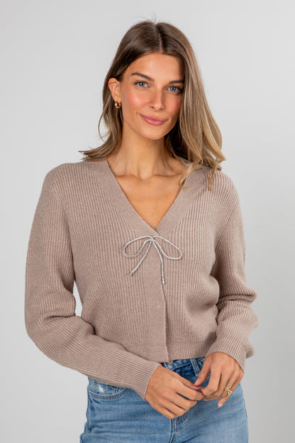 Woman wearing a beige ribbed sweater with a tie detail on a plain background