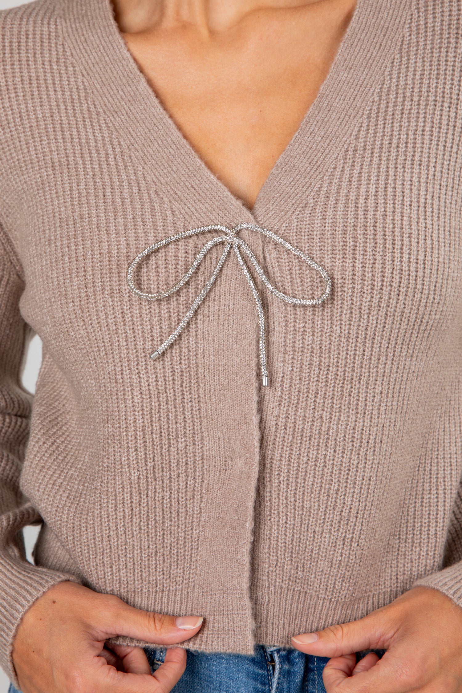 Close-up of a beige cardigan with a bow detail on a blurred background