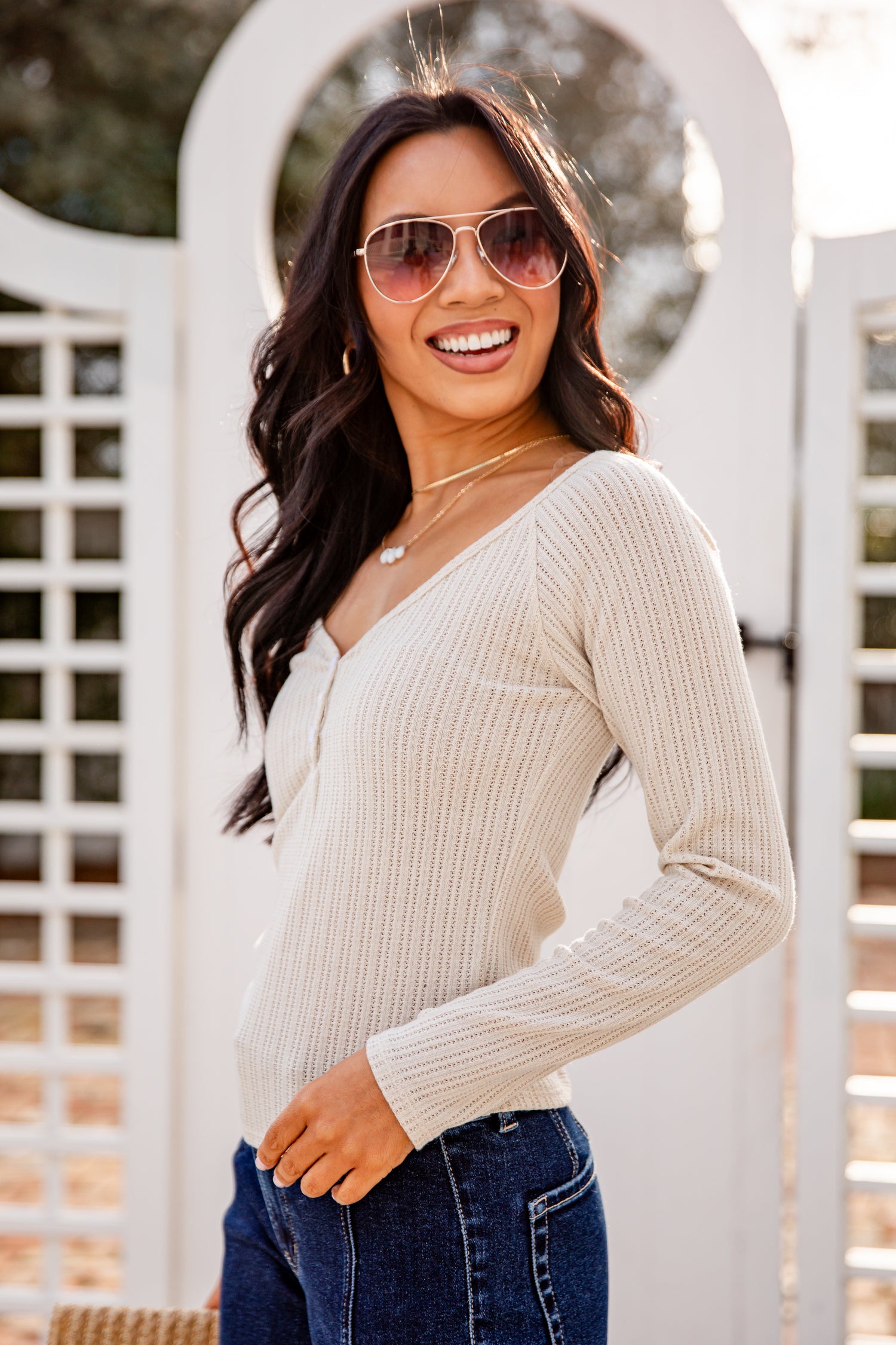 Woman wearing a beige ribbed sweater and sunglasses outdoors.