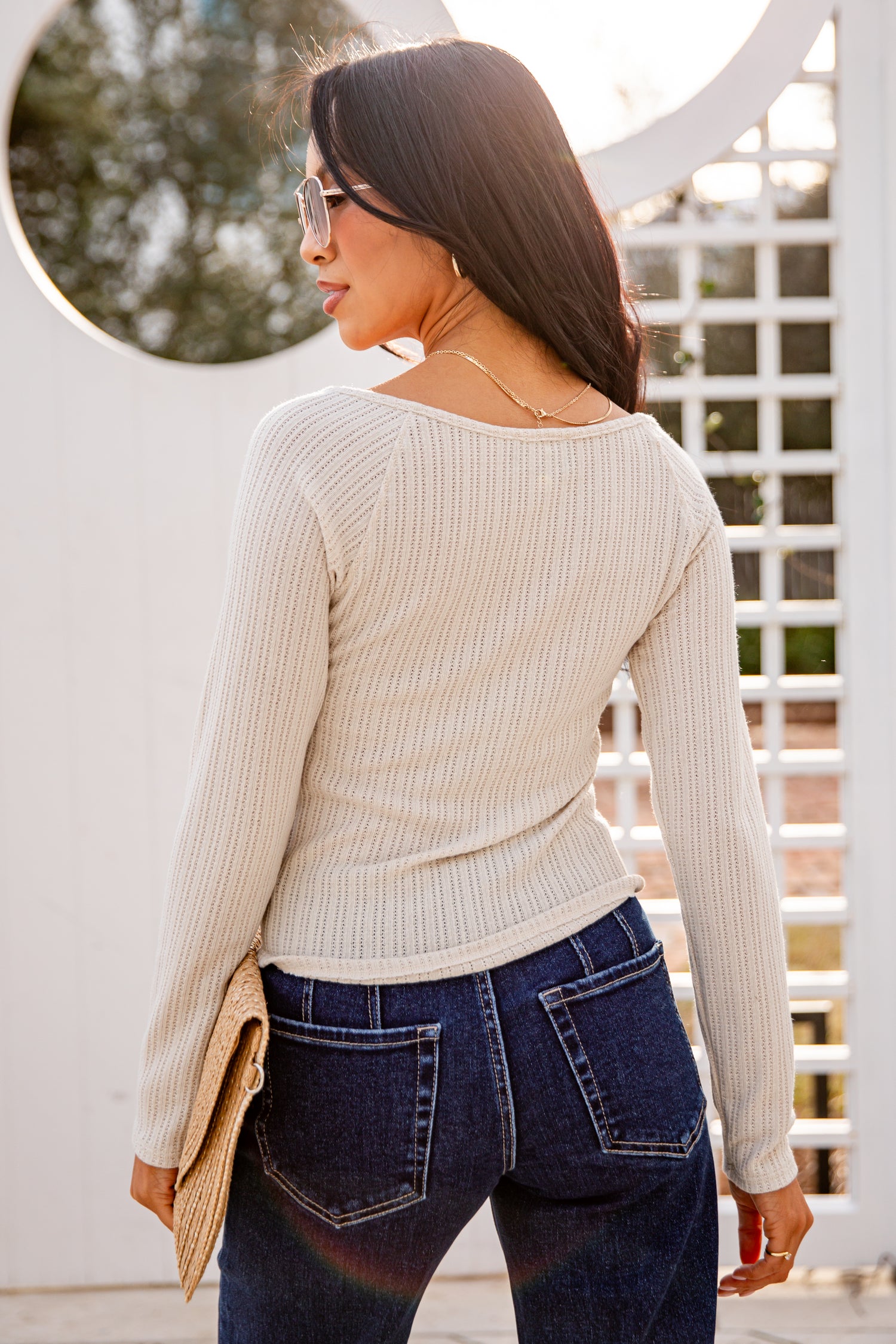 Woman wearing a beige sweater and blue jeans standing outdoors.