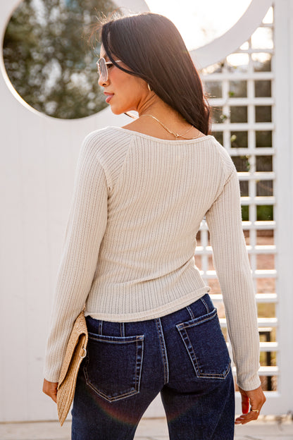 Woman wearing a beige sweater and blue jeans standing outdoors.