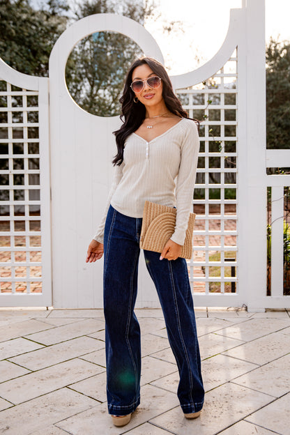 Woman wearing a white blouse, blue jeans, and sunglasses standing in front of a white lattice fence.