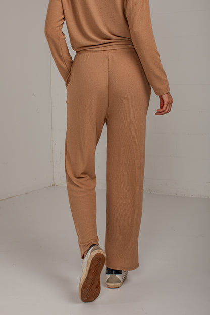 A person shown from the back wearing a matching ribbed knit two-piece set in a warm camel brown, featuring a long-sleeve top and wide-leg pants, paired with white sneakers.