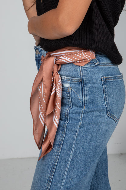 Person wearing a black top and blue jeans with a patterned scarf around their waist against a white background