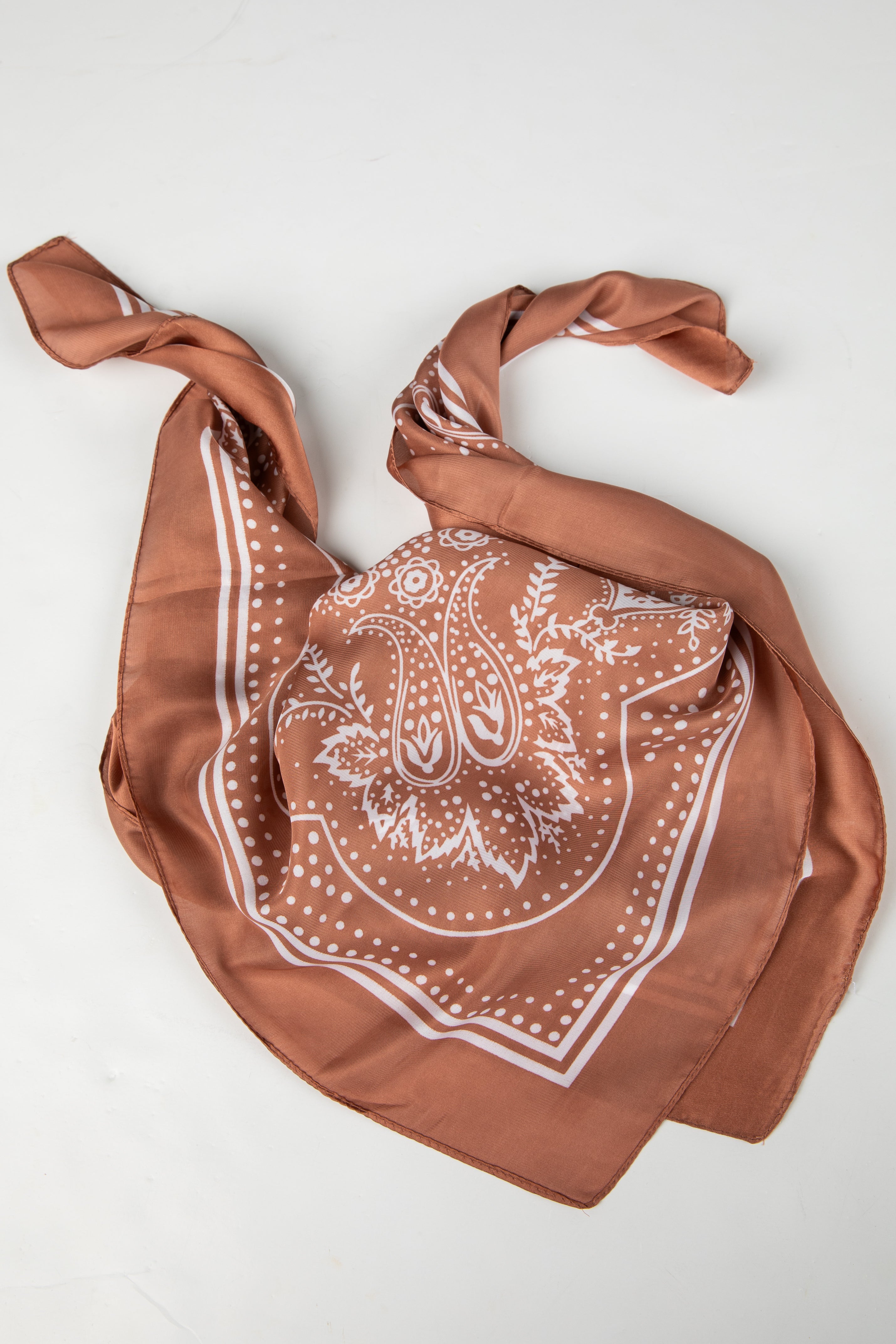 Brown bandana with white paisley pattern on a light gray background