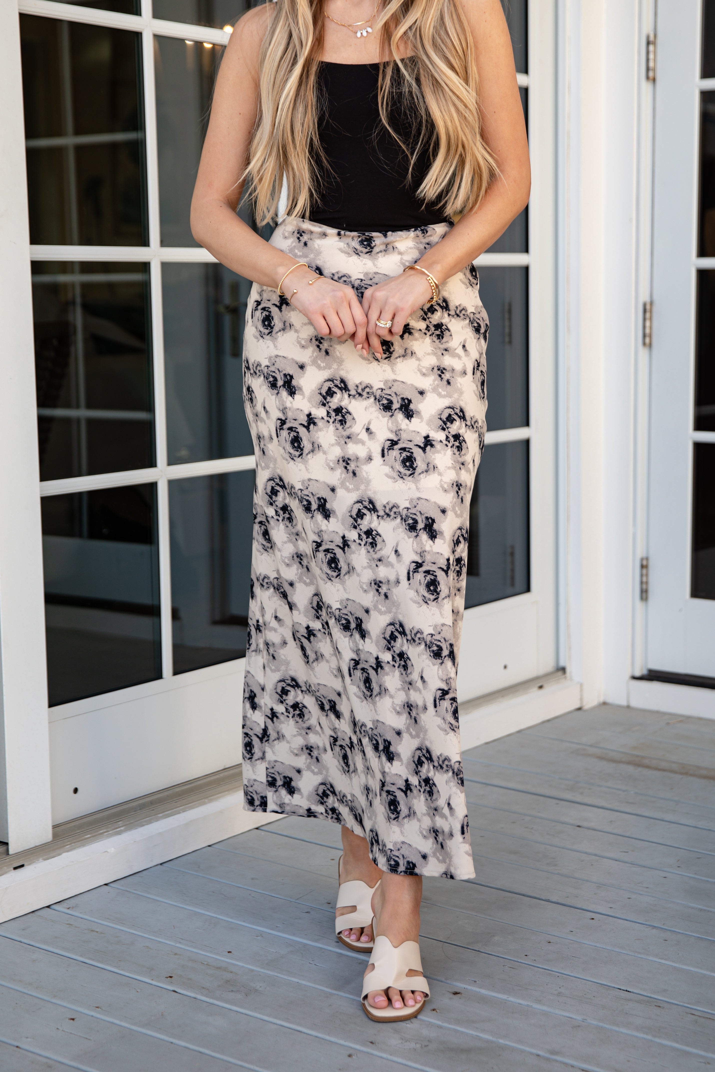 Woman wearing a black top and floral skirt on a wooden deck.