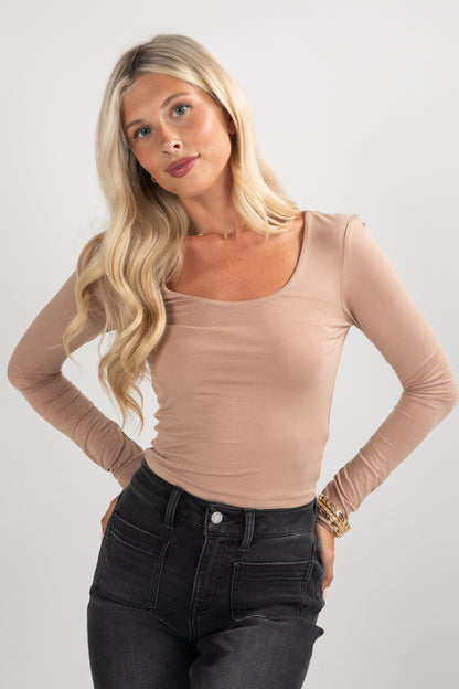 Woman wearing a beige long-sleeve top and black jeans on a white background