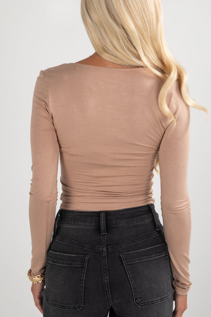 Person wearing a beige long-sleeve top and black pants on a white background