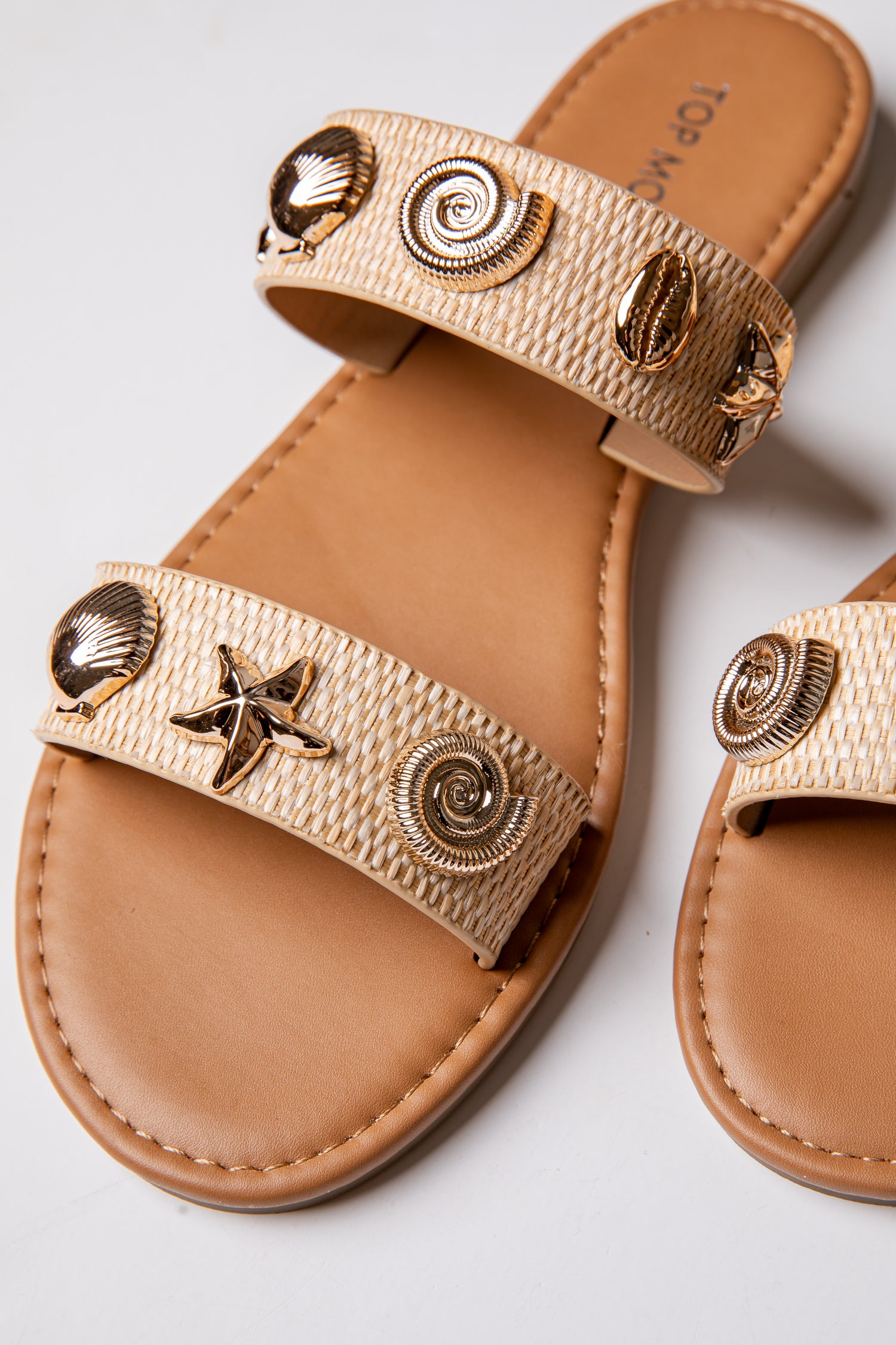 Tan sandals with decorative straps featuring shells and a star on a light gray background