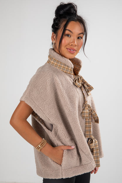 Woman wearing a beige fleece vest with plaid accents on a white background