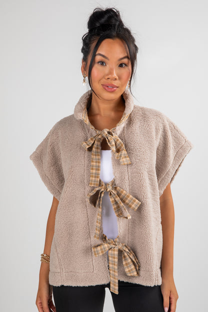 Woman wearing a beige fleece vest with plaid tie details on a white background