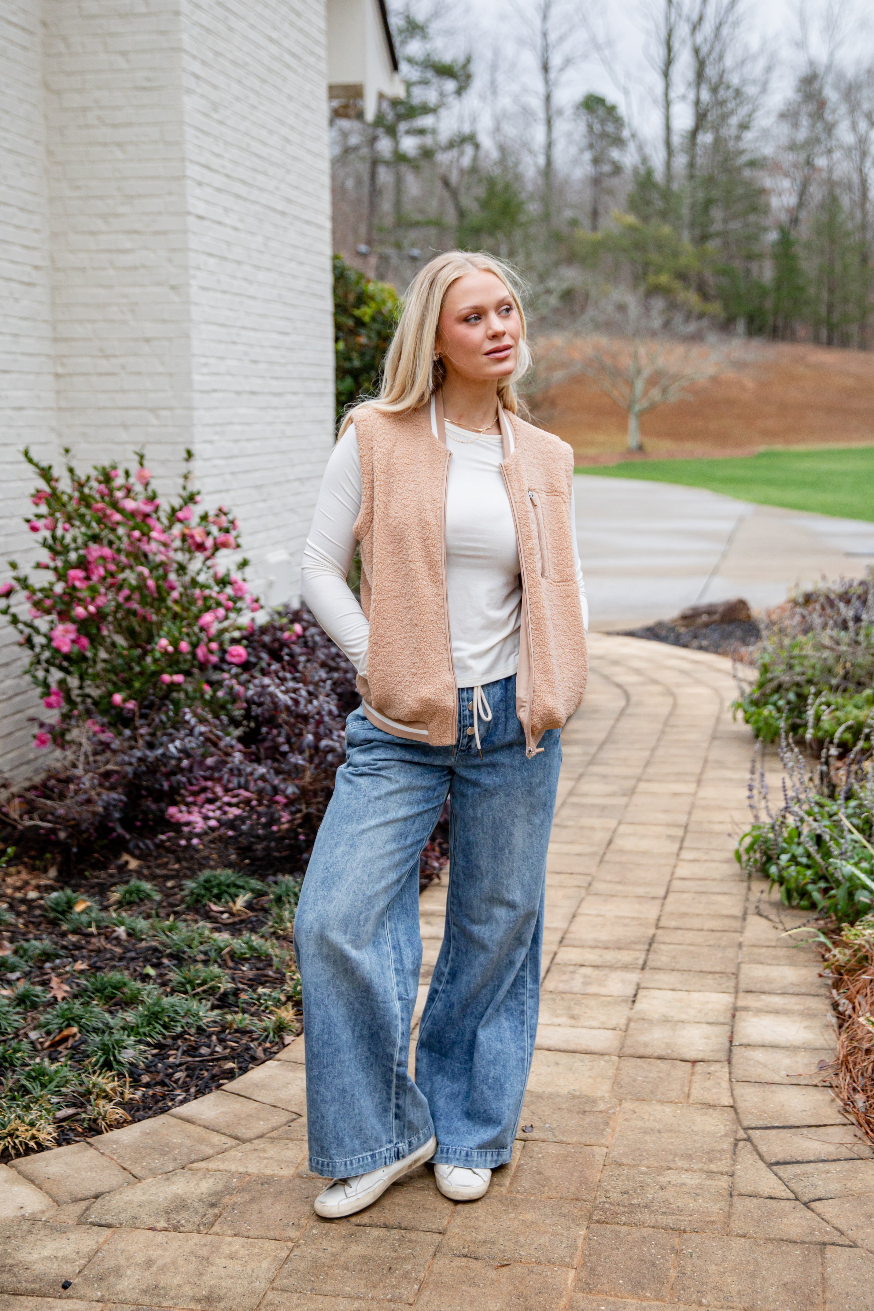 Woman standing on a paved walkway with a garden and house in the background