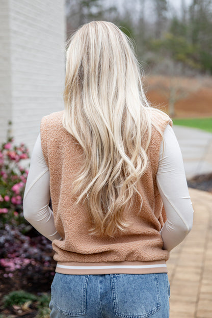 Person wearing a beige vest with long blonde hair, standing outdoors.