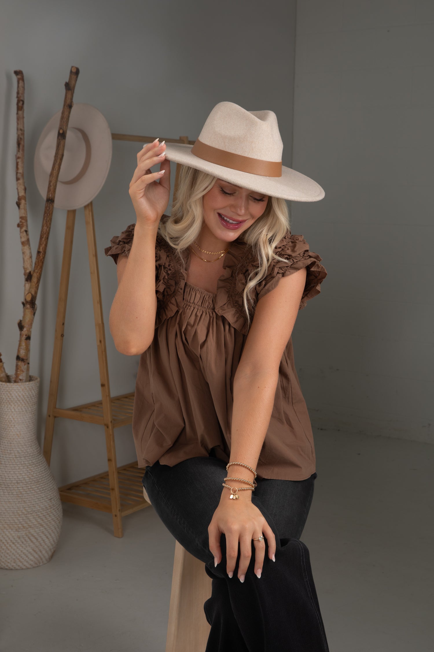 Woman wearing a brown top and beige hat in a studio setting with a gray background