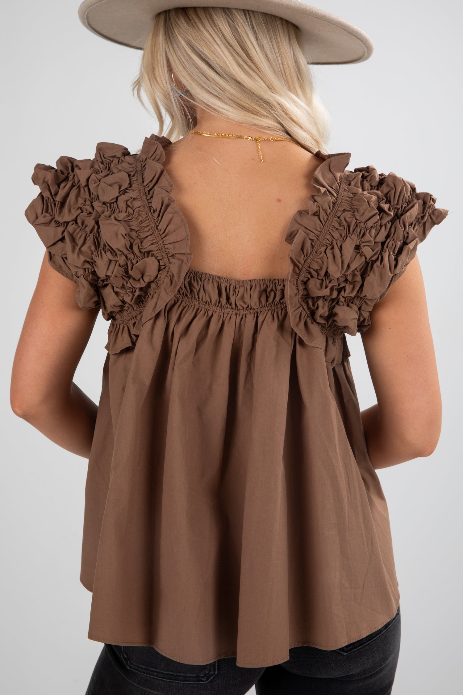 Brown ruffled top worn by a person on a plain background