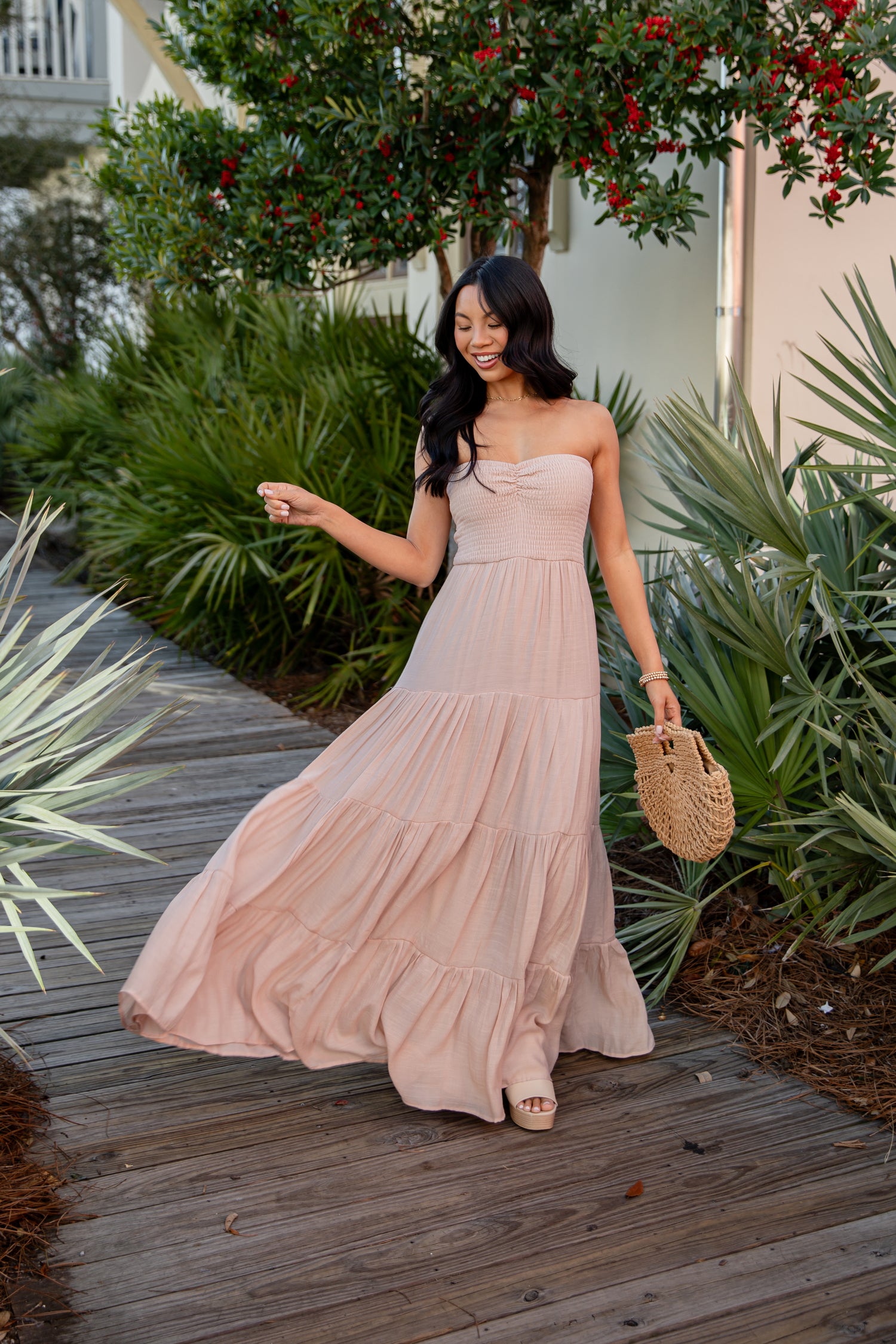 Woman in a long beige dress standing on a wooden path with greenery around.