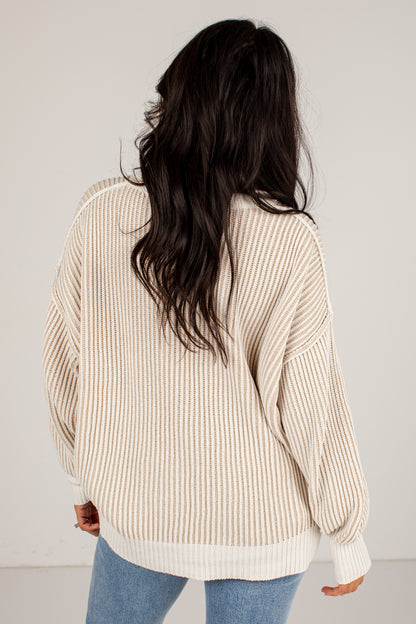 A woman viewed from behind wearing a cream and beige vertically striped knit sweater with balloon sleeves, paired with light blue jeans, against a plain off-white background.