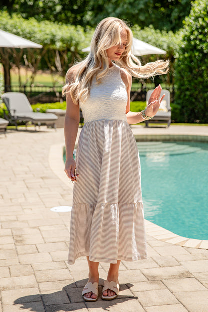 Woman in a light dress standing by a pool with greenery in the background